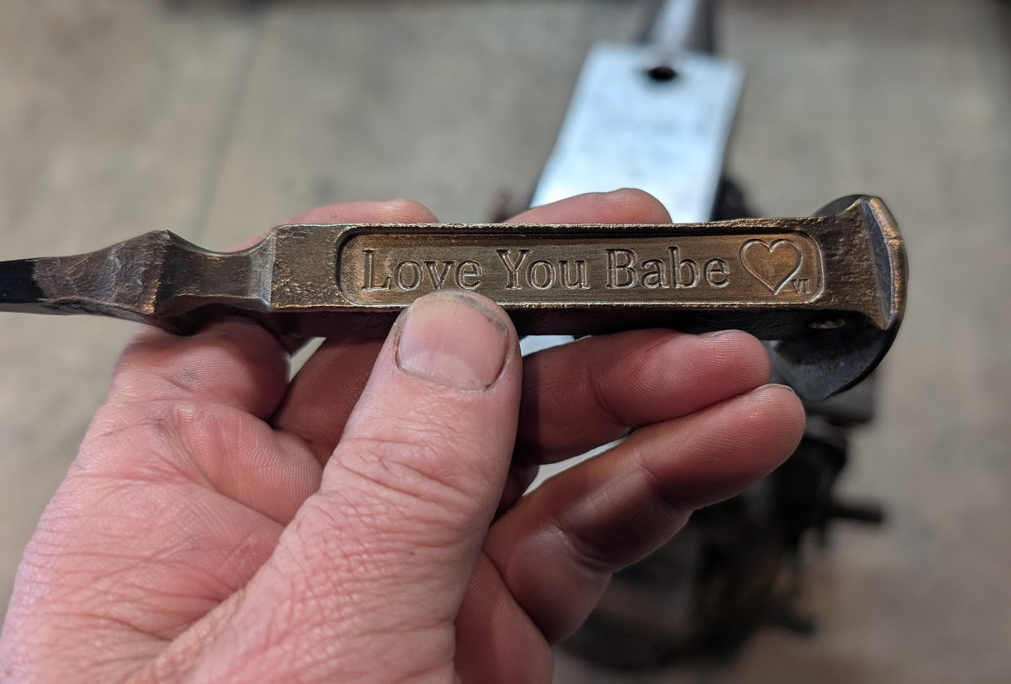 Hand holding a metal object engraved with 'Love You Babe' and a heart symbol.