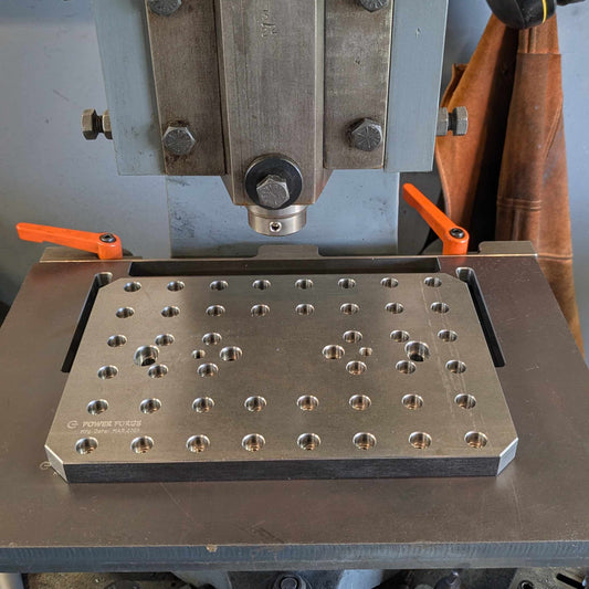 Metalworking machine with a metal plate featuring drilled holes on a workshop background