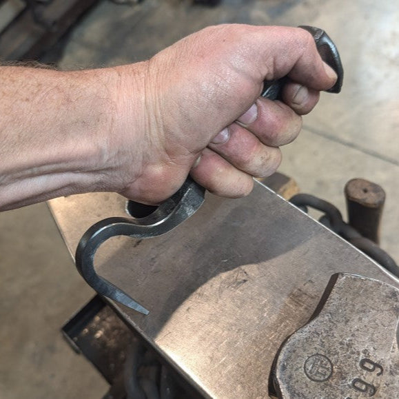 Hand holding a large metal hook on a workshop surface