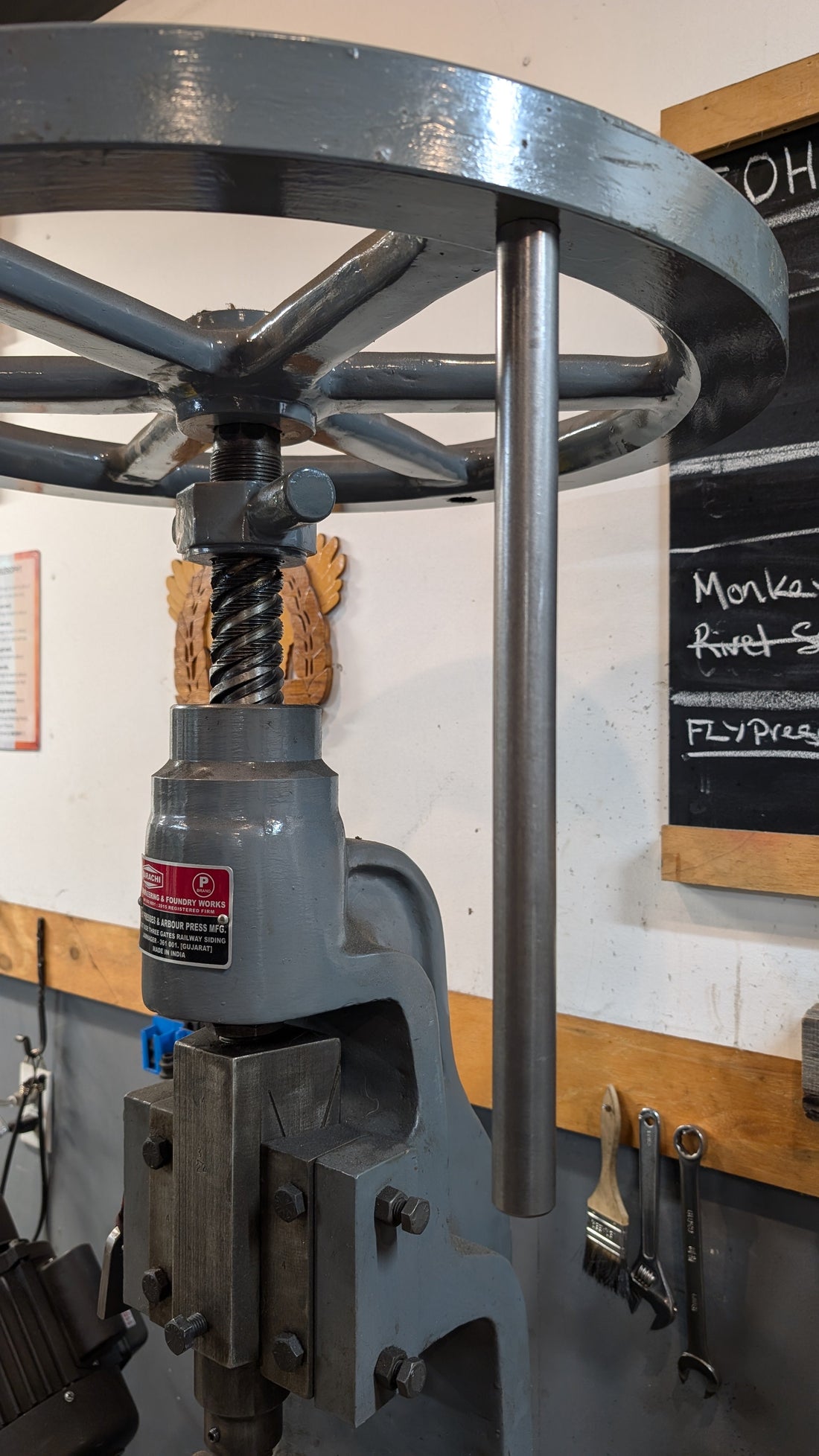 Bare-metal handle rod installed beneath the flywheel of the Karachi fly press.