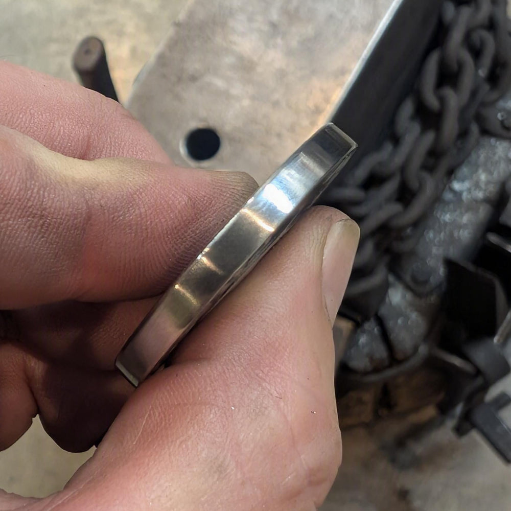 A close-up of a hand holding a polished, brushed metal Stainless Steel Coin.