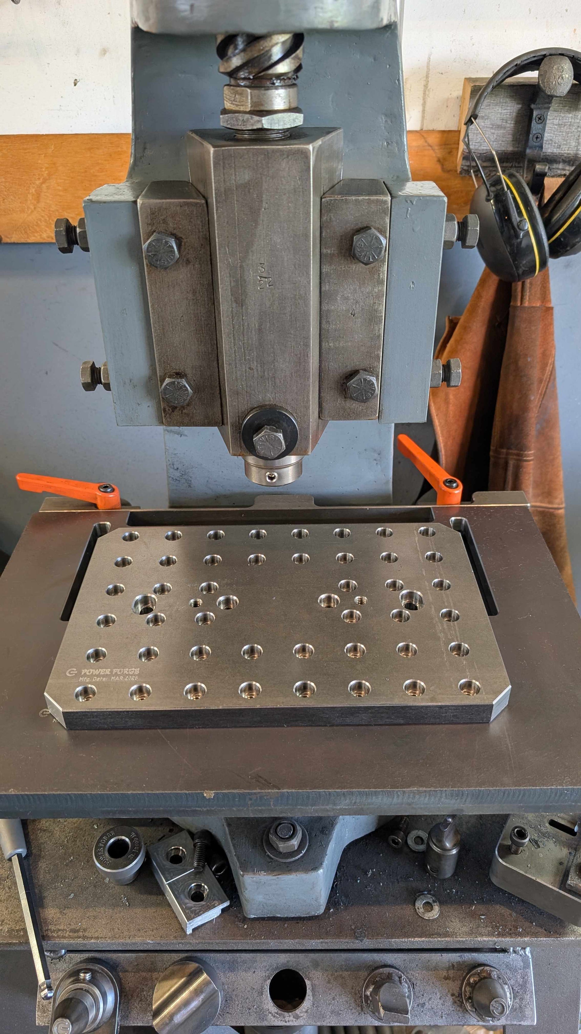 Metalworking machine with a metal plate featuring drilled holes on a workshop background