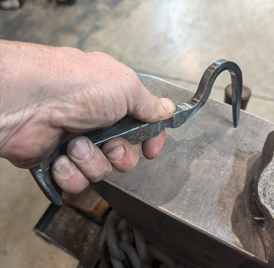 Hand holding a metal tool over a anvil in a workshop setting