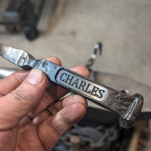 Metal tool with 'CHARLES' engraving held by a hand, blurred background