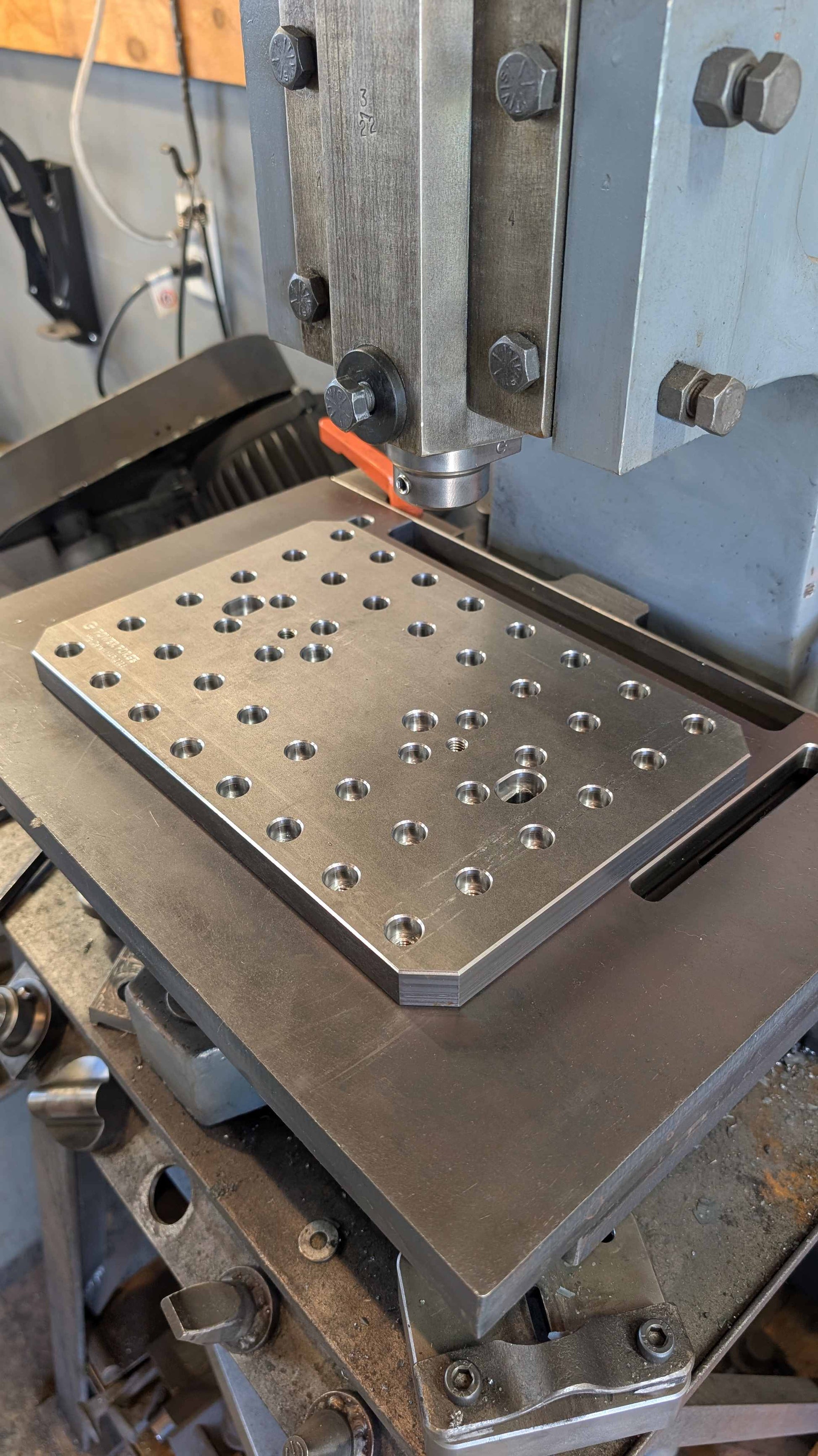 Metalworking machine with a metal plate featuring holes on a workshop background